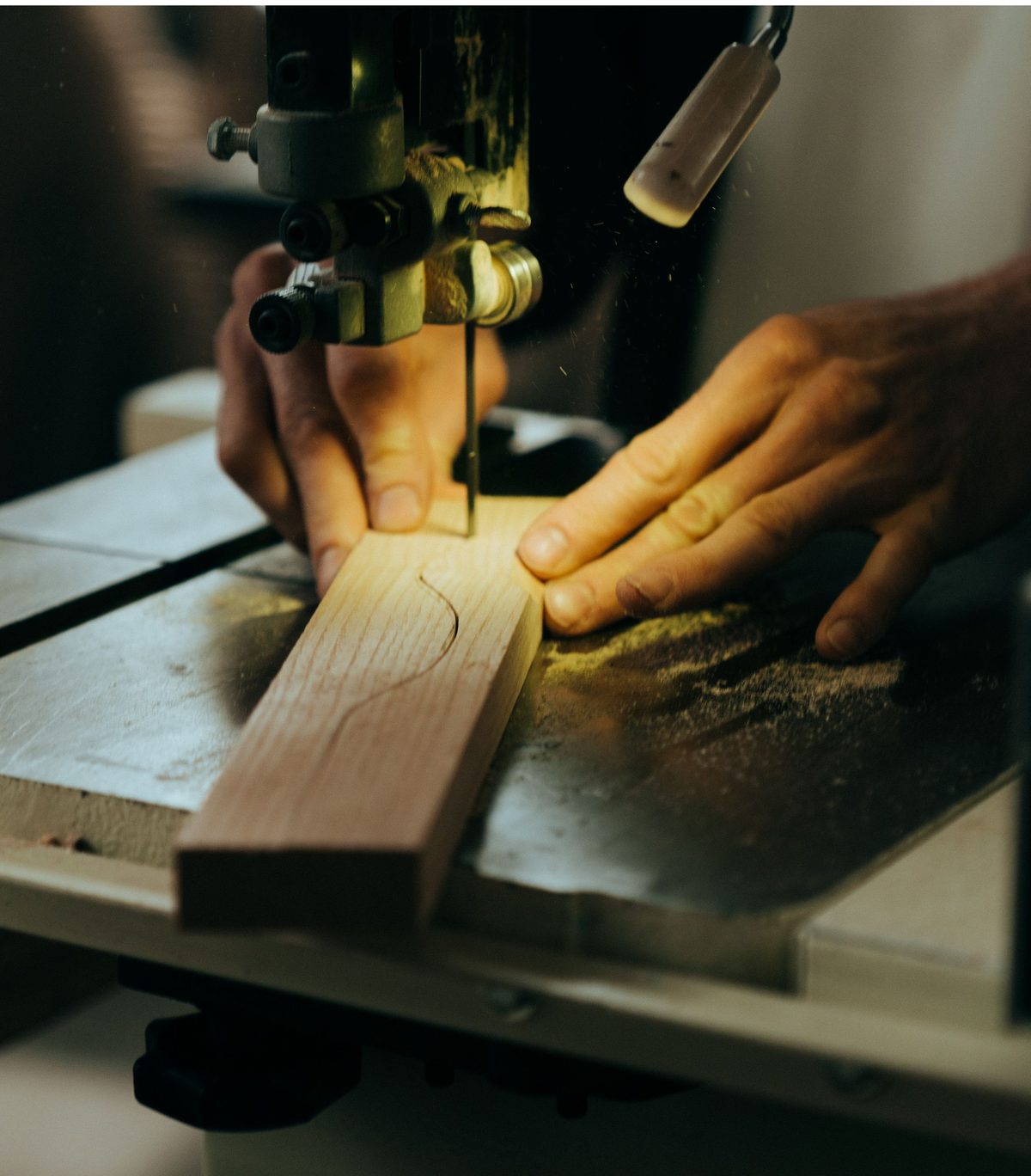 Hands guiding a timber strip along a marked curve at a band saw